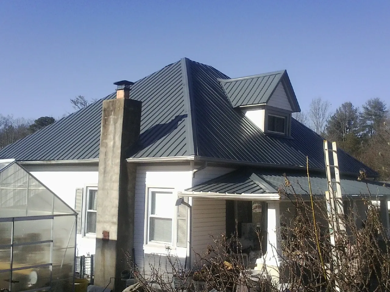 Dark blue standing seam metal roof on a white farmhouse with dormer — Slate & Tile Roof Repair by Roofing Brothers in Malo