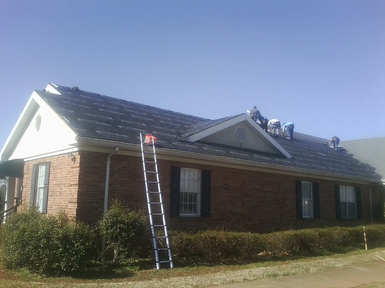 Crew tearing shingles off a brick ranch roof with a ladder set — Emergency Roof Repair work by our crew in Malo