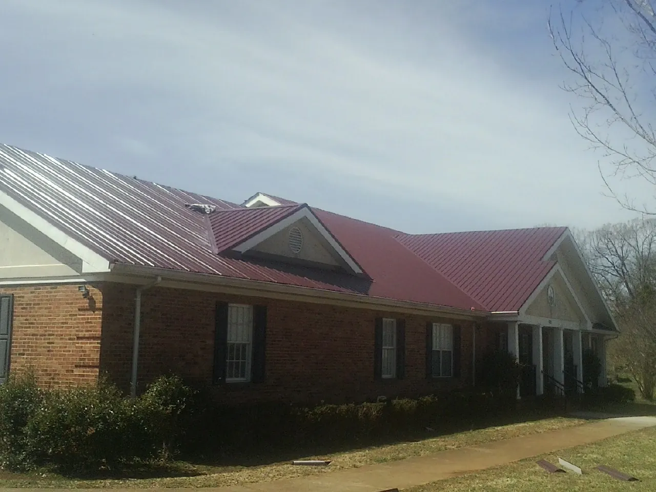 Red metal roof with gabled entries on a long brick building, from a Hail Damage Roof Repair job in Malo