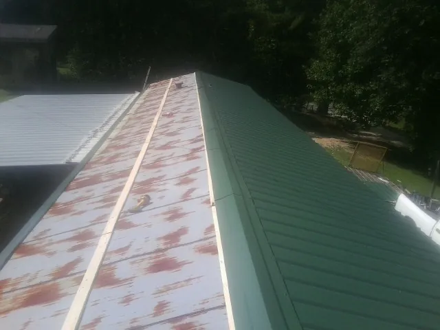 Old rusted panels beside newly installed green metal roofing — Wind Damage Roof Repair by Roofing Brothers in Malo