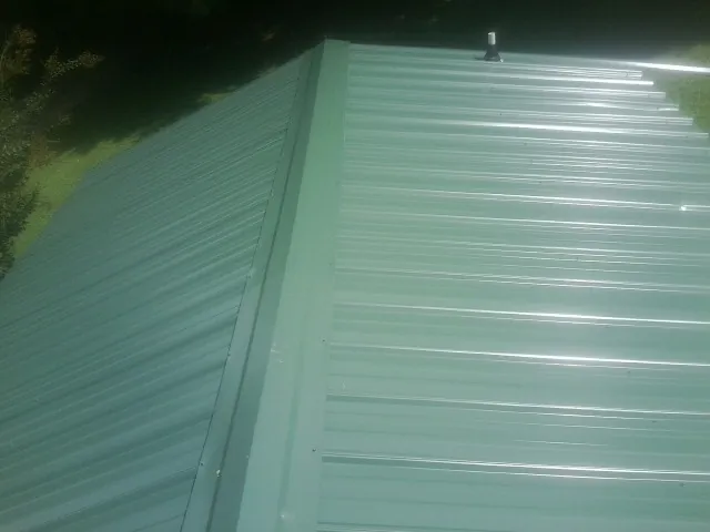 New green metal panels meeting at the ridge of a roof — Flat Roof Repair work by our crew in Malo