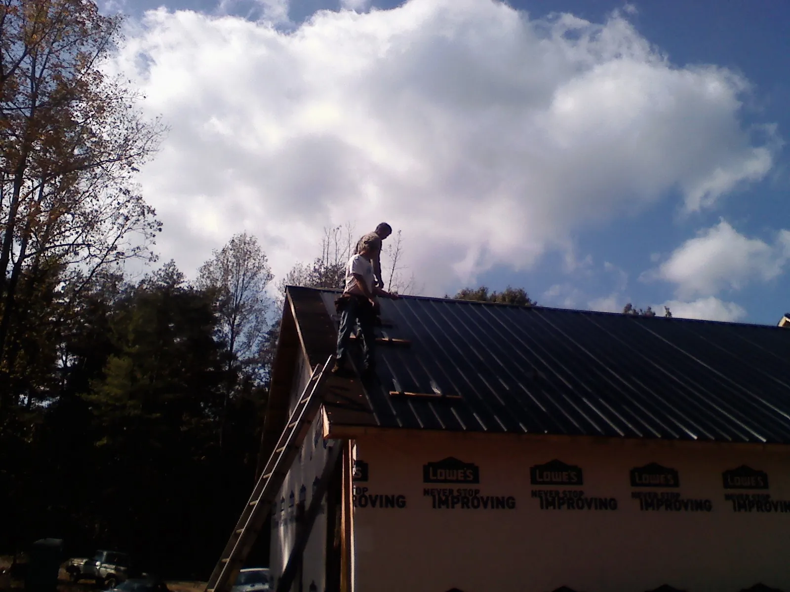 Roofer fastening dark metal panels high against a cloudy sky, from a Roof Inspection job in Malo