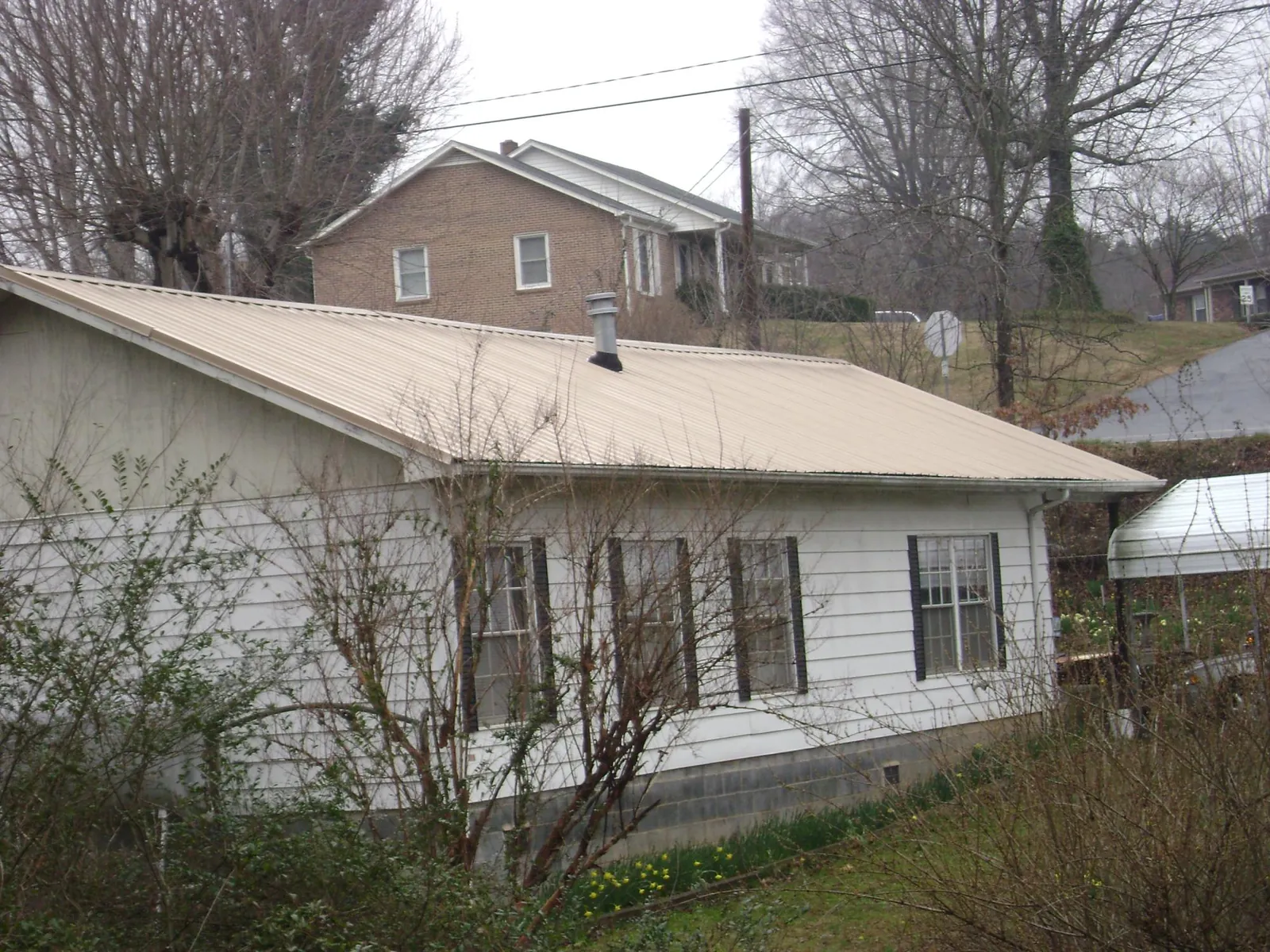 Tan metal roof on a white sided house set into a hillside — Commercial Roofing by Roofing Brothers in Malo